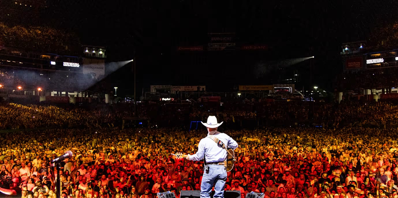 A country artist in a white cowboy hat and jeans faces a massive sold-out crowd at Nissan Stadium during CMA Fest in Nashville.