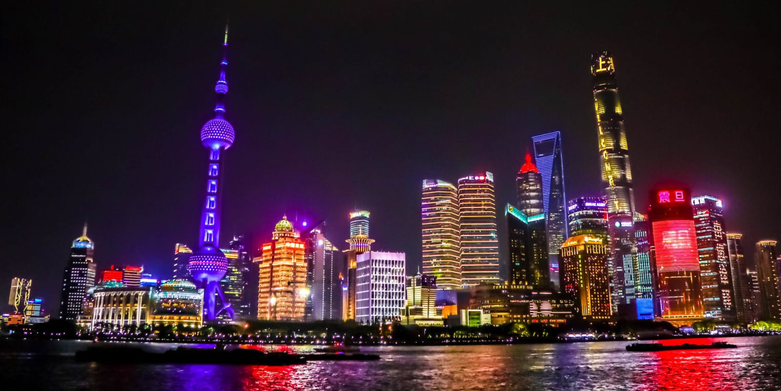 The illuminated Pudong skyline at night, with the Oriental Pearl Tower glowing purple over the Huangpu River in Shanghai.