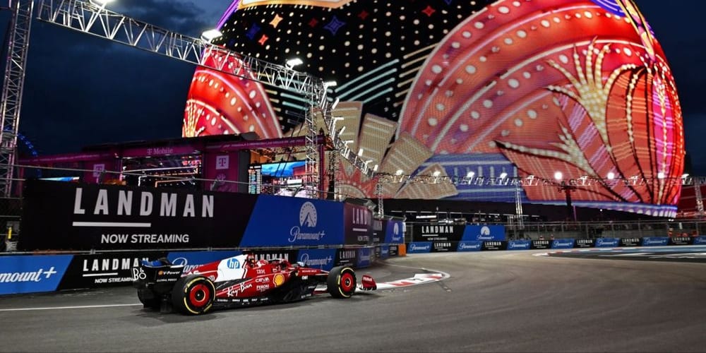A Ferrari F1 car racing past the illuminated Sphere displaying the Welcome to Las Vegas sign during the Formula 1 Las Vegas Grand Prix at night.