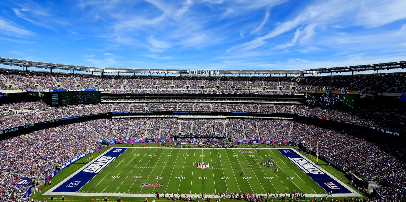Aerial view of a sold-out New York Giants game at MetLife Stadium in East Rutherford, New Jersey, under a bright blue sky.