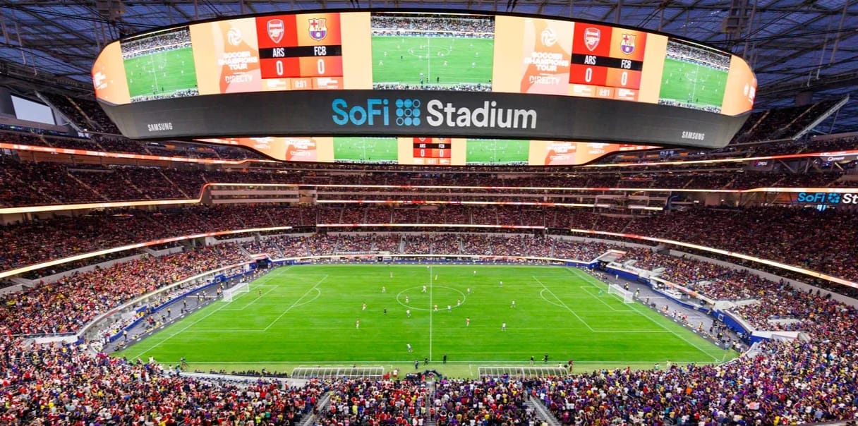 A sold-out soccer match between Arsenal and Barcelona at SoFi Stadium in Los Angeles, with the venue's massive circular scoreboard overhead.