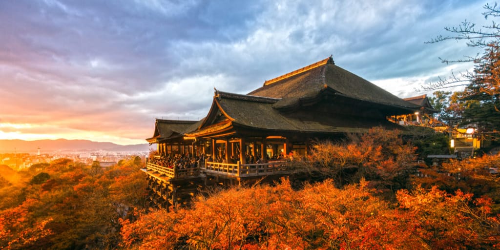 Kiyomizu-dera Temple's wooden stage overlooking a hillside of vivid autumn foliage at sunset in Kyoto, Japan.